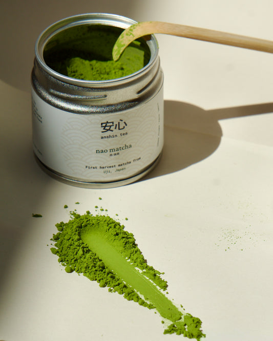 Canister of matcha green tea powder with a wooden spoon on a light background